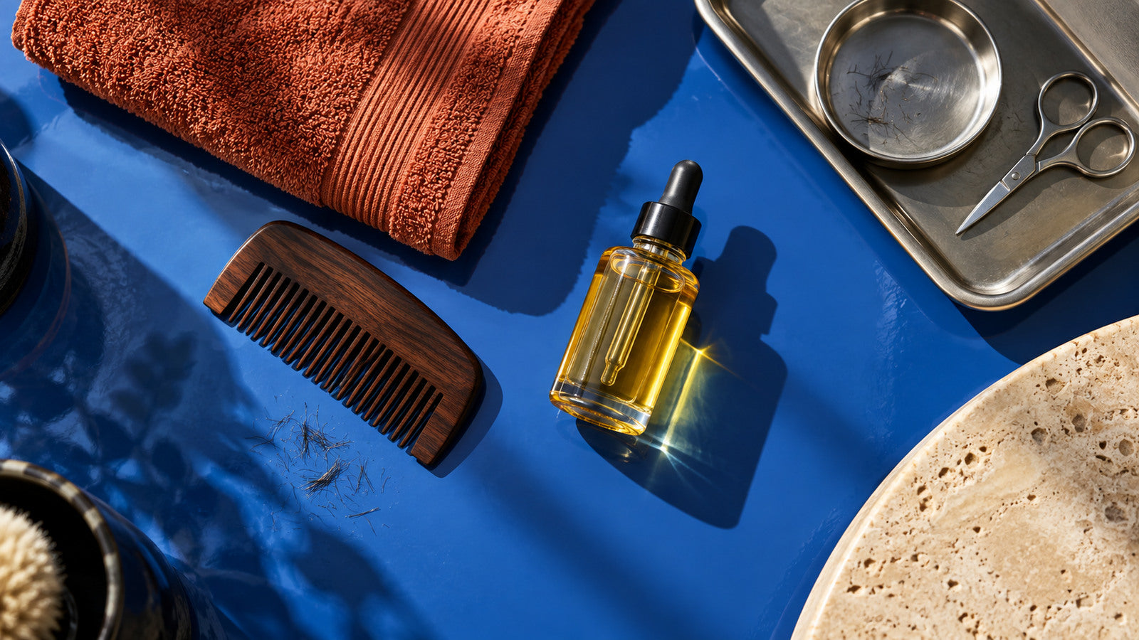 Huile à barbe, peigne en bois et serviette terracotta sur fond bleu cobalt